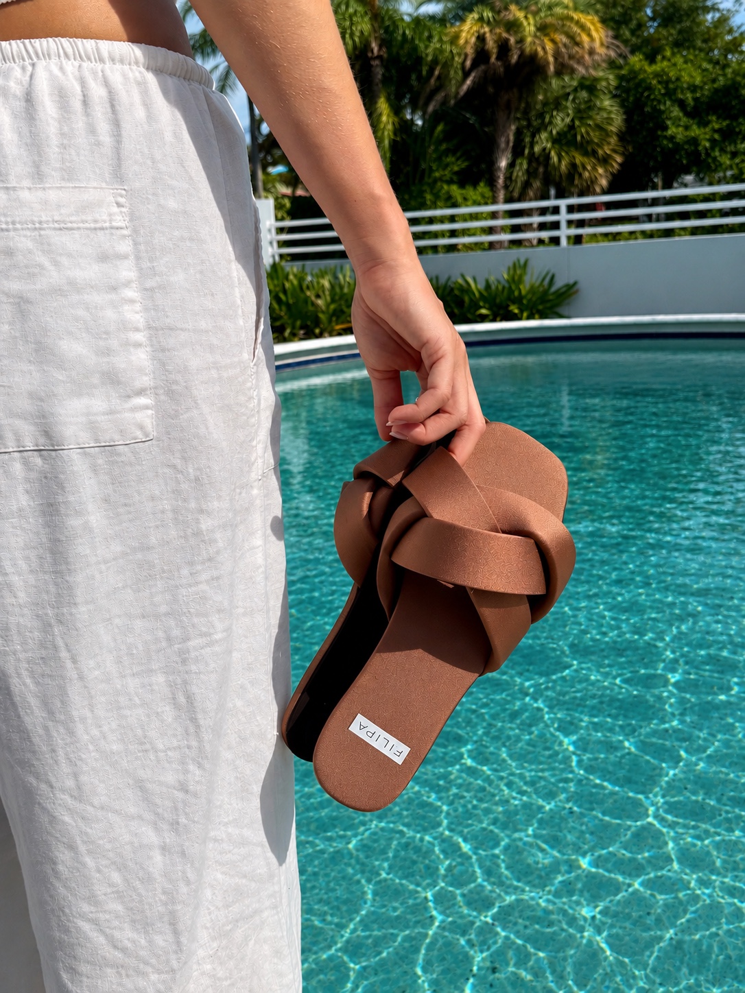Close product detail of brown sandals held beside a pool