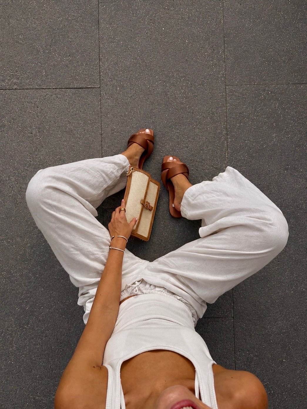 Brown sandals styled with an all-white outfit and woven handbag